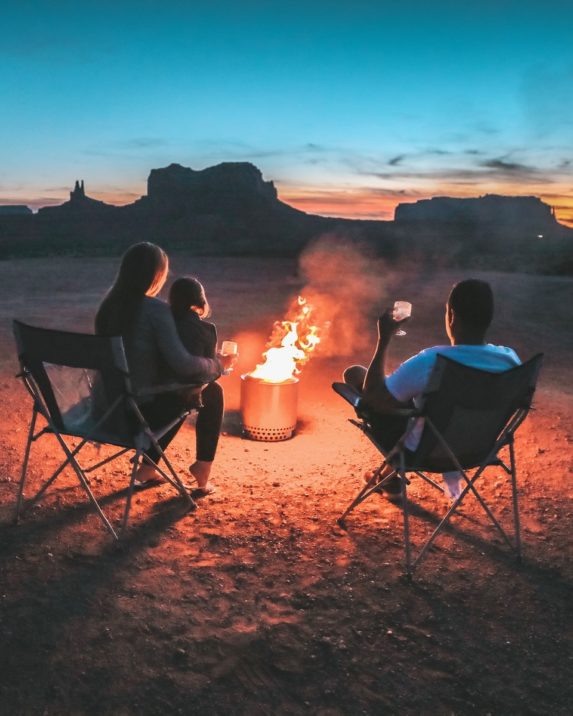 A family watches a sunset around a fire pit in the desert.